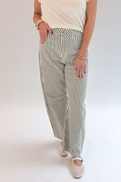 Front detail view of woman wearing Swagger Boutique’s top with Olive Striped Barrel Jeans by Just Black Denim against white studio background.