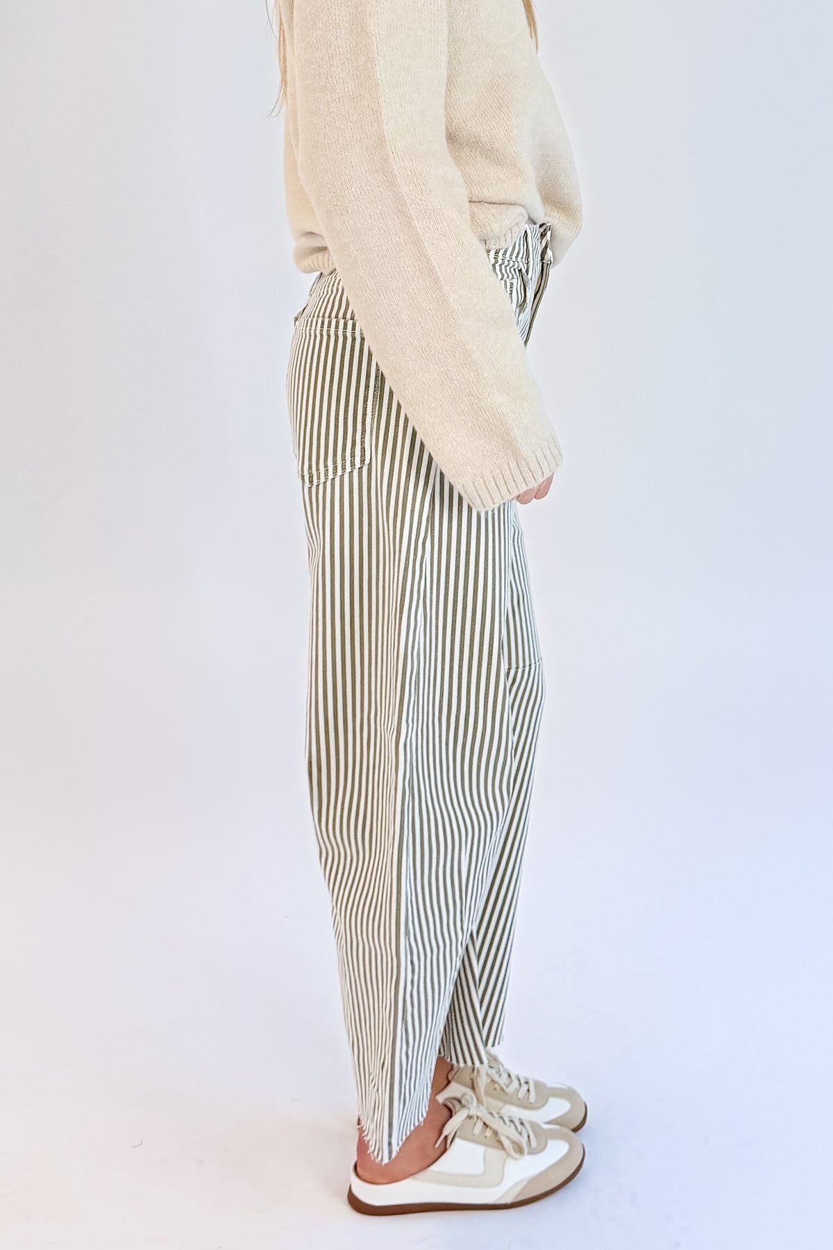 Side detail view of woman wearing Swagger Boutique’s top with Olive Striped Barrel Jeans by Just Black Denim against white studio background.