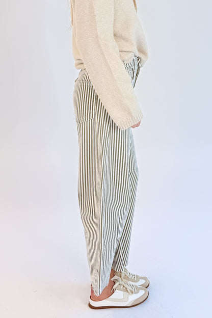 Side detail view of woman wearing Swagger Boutique’s top with Olive Striped Barrel Jeans by Just Black Denim against white studio background.
