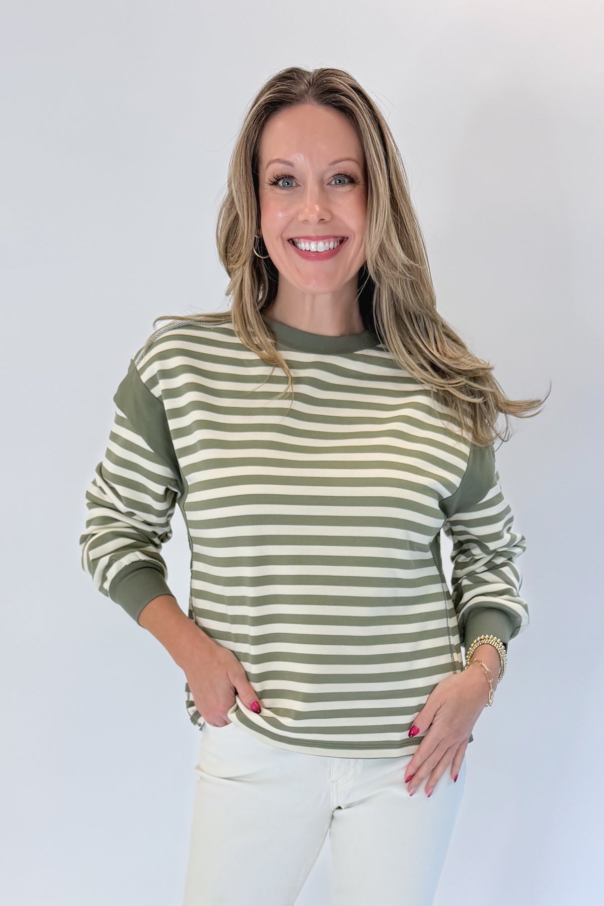 Front view of woman wearing Swagger Boutique’s Olive Striped Sweatshirt with jeans against white studio background.