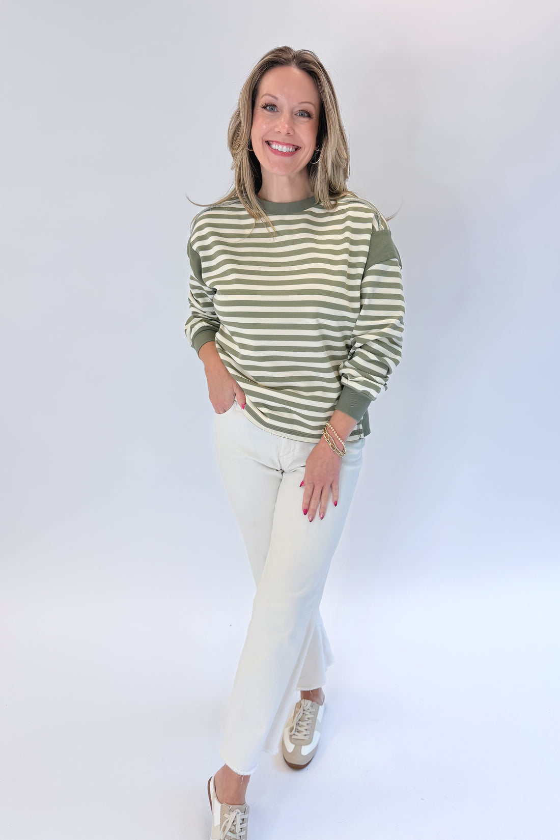 Front view of woman wearing Swagger Boutique’s Olive Striped Sweatshirt with jeans against white studio background.