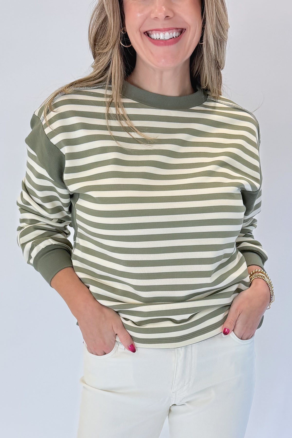 Front detail view of woman wearing Swagger Boutique’s Olive Striped Sweatshirt with jeans against white studio background.