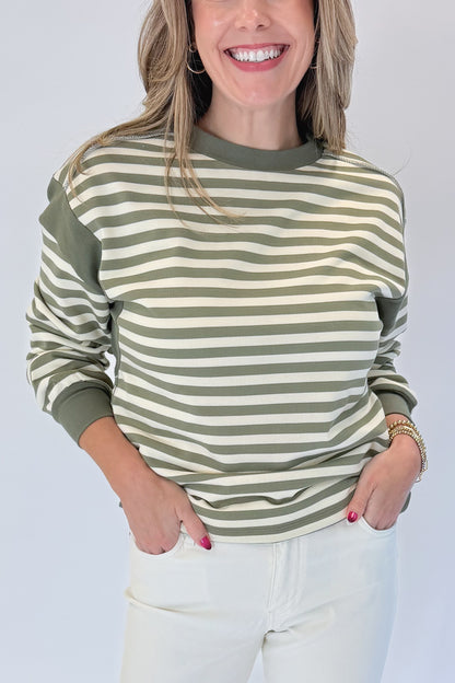 Front detail view of woman wearing Swagger Boutique’s Olive Striped Sweatshirt with jeans against white studio background.