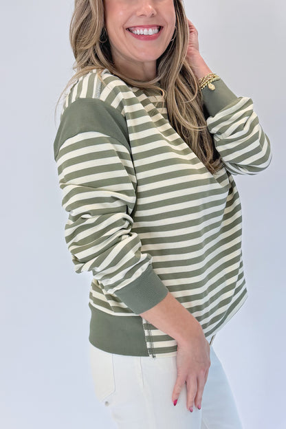Side view of woman wearing Swagger Boutique’s Olive Striped Sweatshirt with jeans against white studio background.