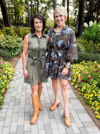 Front view of women wearing Swagger Boutique’s Brown &amp; Blue Floral Tie Waist Mini Dress and Olive Suede Dress standing outside by a garden.