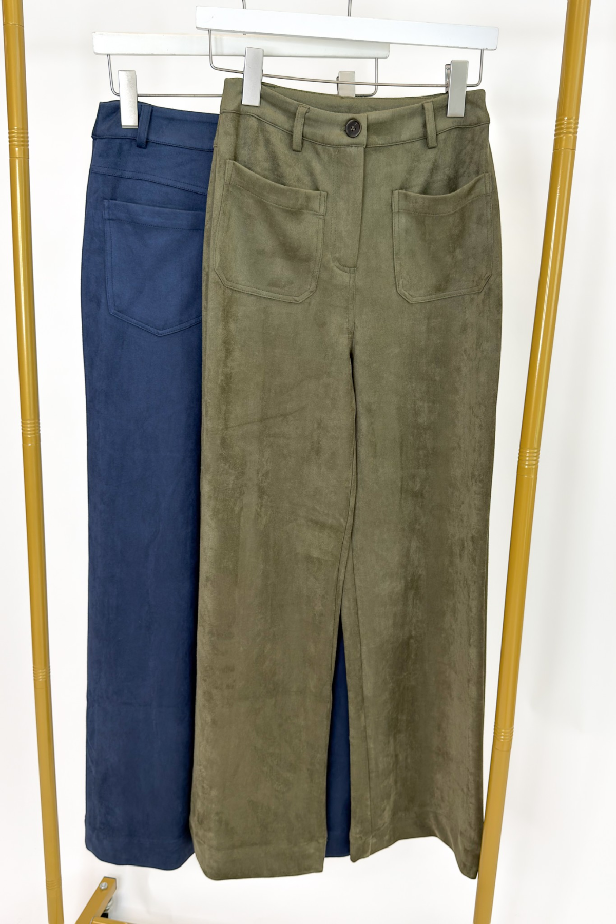 Swagger Boutique’s sweater with Olive Suede Wide Leg Pants and Navy Suede pants hanging against white studio background.