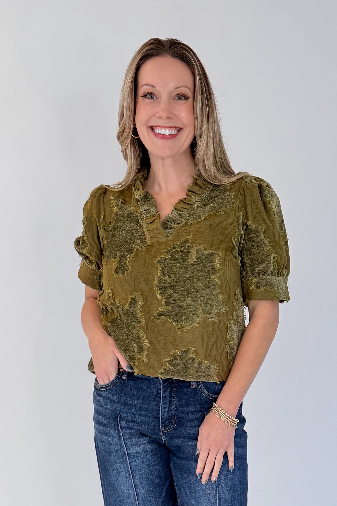 Front view of woman wearing Swagger Boutique’s Olive Velvet Ruffle Neck Top with jeans against white studio background.