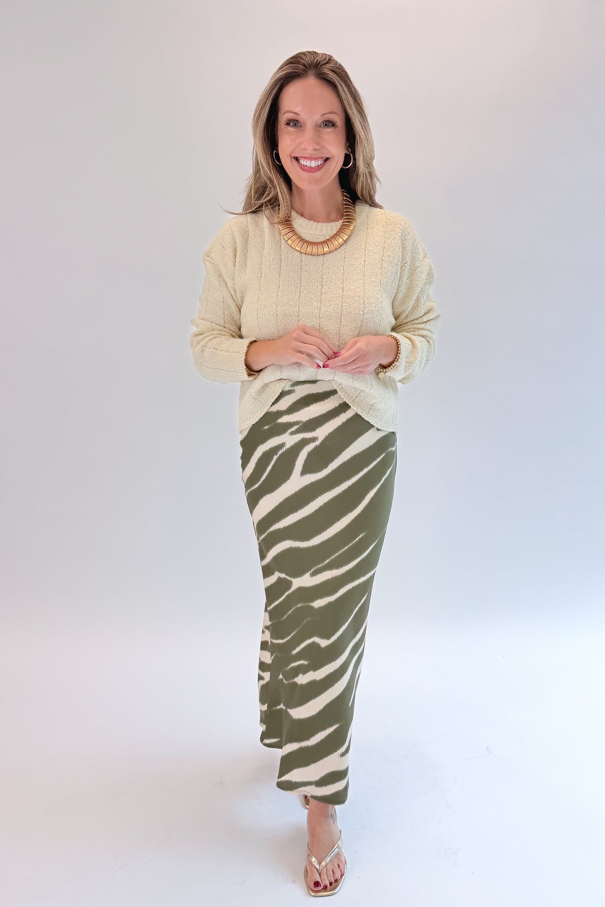 Front view of woman wearing Swagger Boutique’s Olive Zebra Print Satin Skirt with sweater against white studio background.