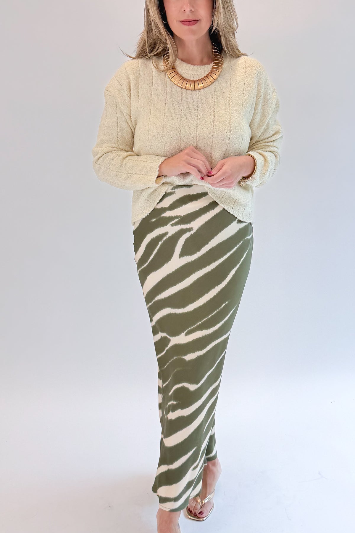Front detail view of woman wearing Swagger Boutique’s Olive Zebra Print Satin Skirt with sweater against white studio background.