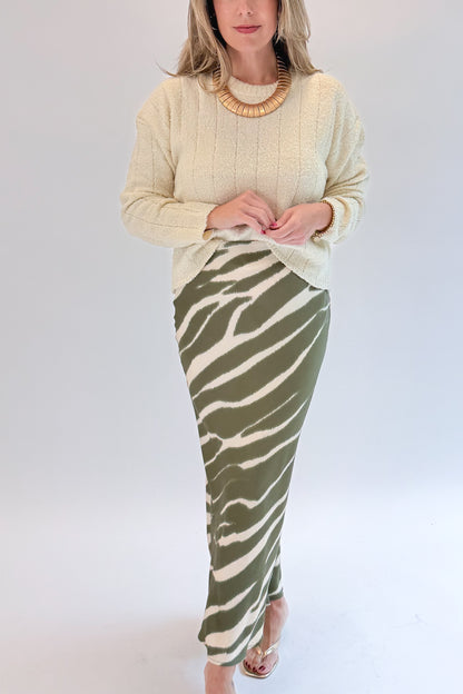 Front detail view of woman wearing Swagger Boutique’s Olive Zebra Print Satin Skirt with sweater against white studio background.