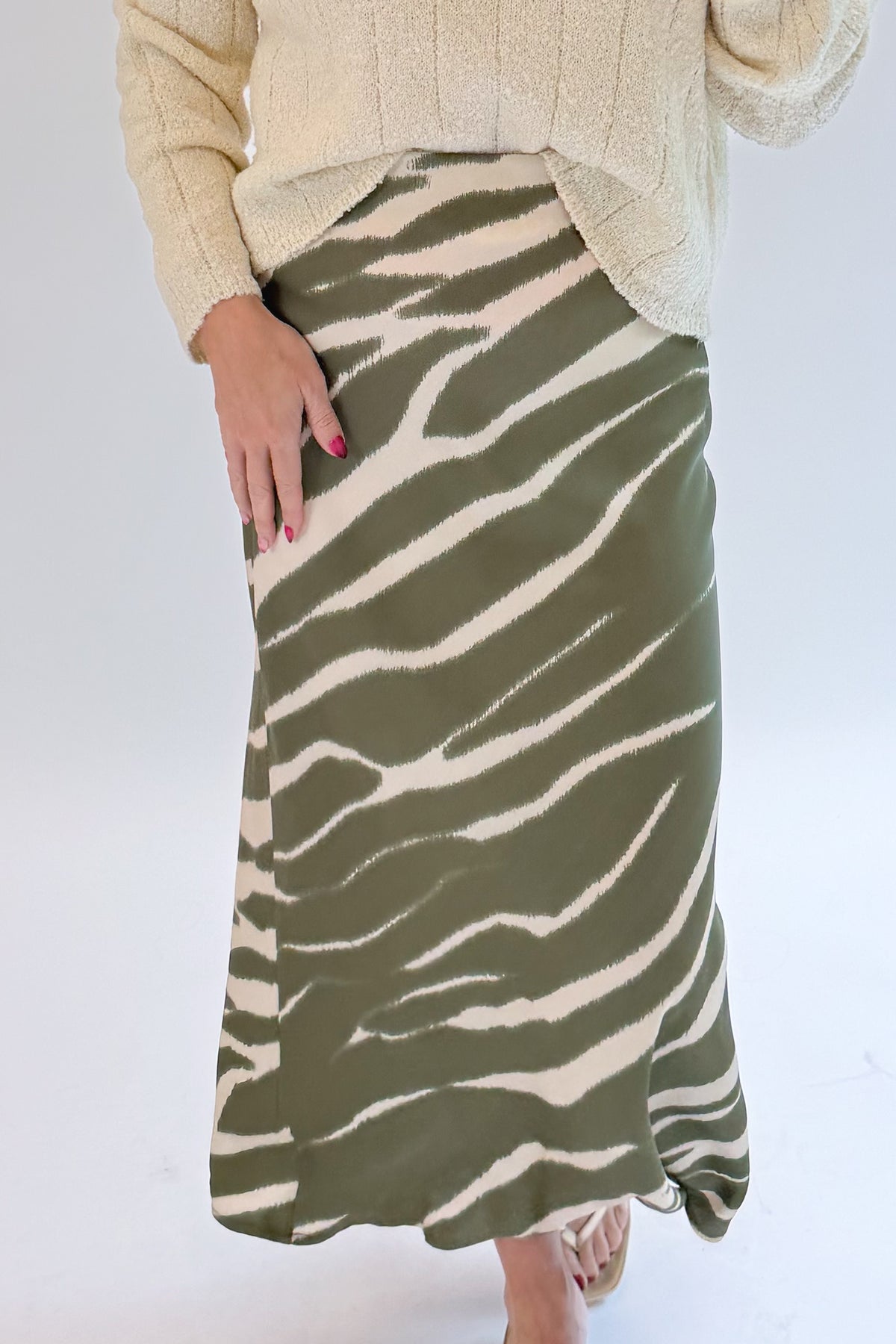 Front detail view of woman wearing Swagger Boutique’s Olive Zebra Print Satin Skirt with sweater against white studio background.