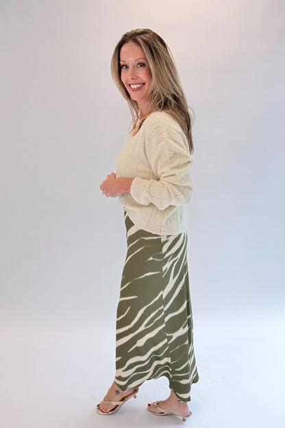 Side view of woman wearing Swagger Boutique’s Olive Zebra Print Satin Skirt with sweater against white studio background.