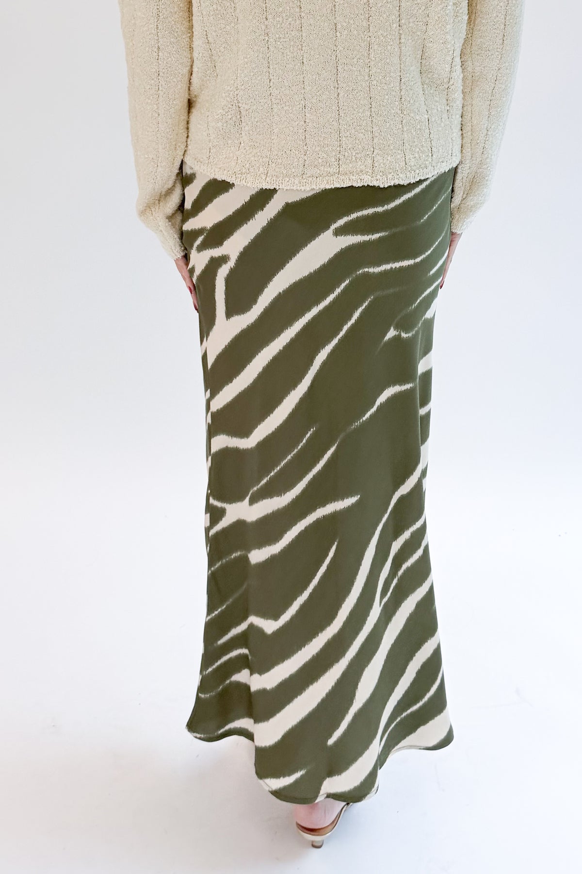 Back view of woman wearing Swagger Boutique’s Olive Zebra Print Satin Skirt with sweater against white studio background.