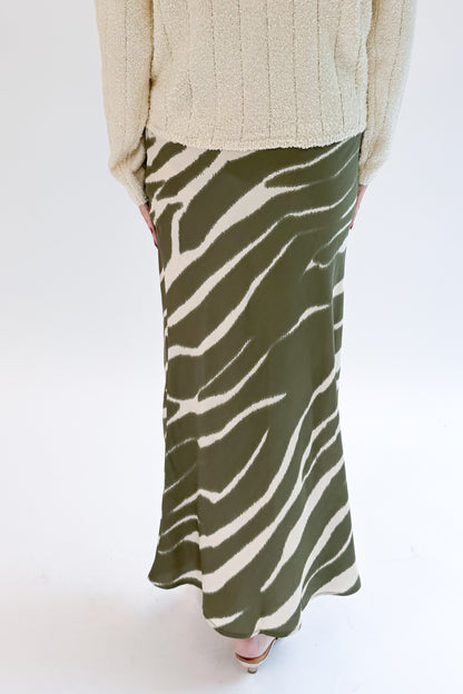 Back view of woman wearing Swagger Boutique’s Olive Zebra Print Satin Skirt with sweater against white studio background.