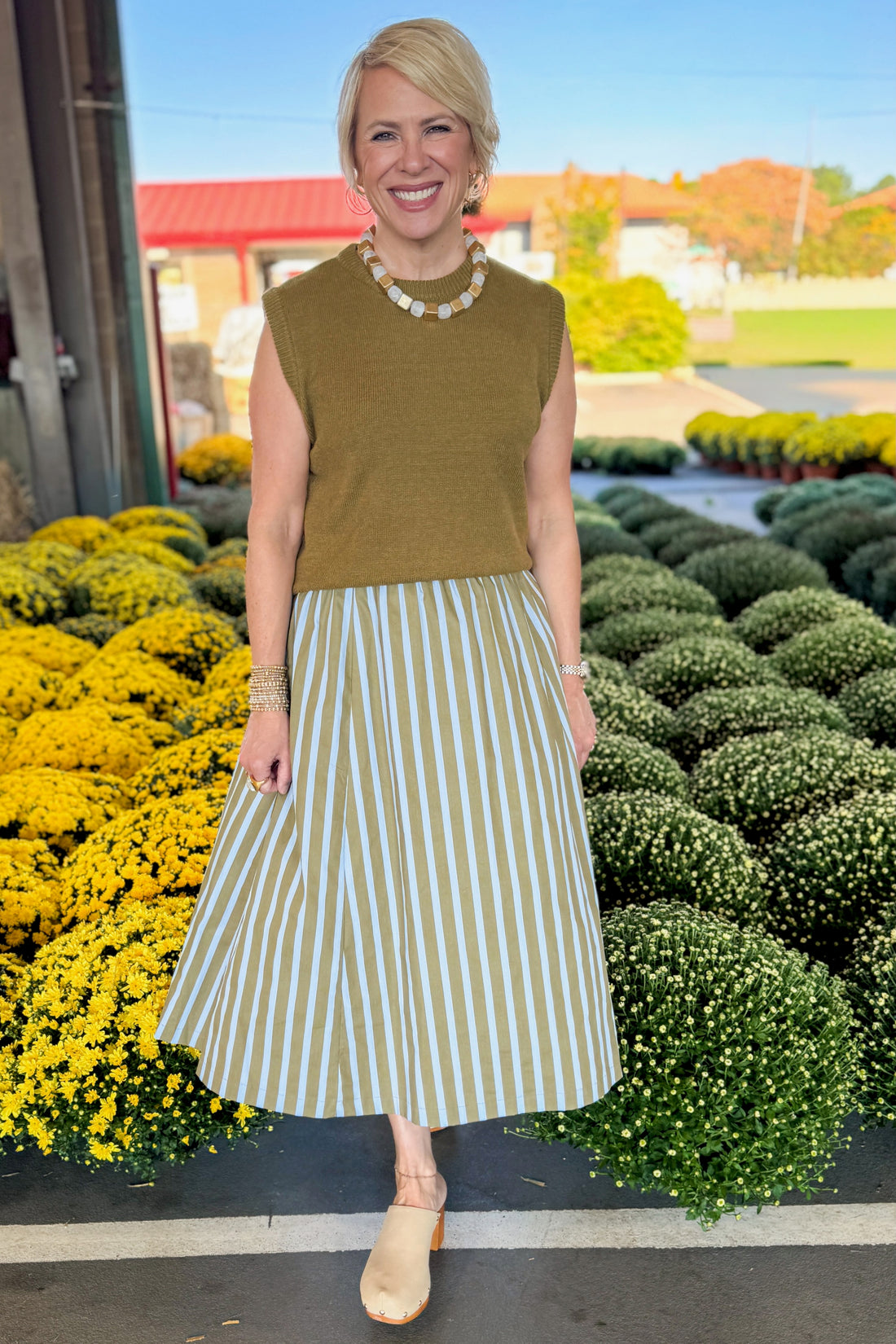 Front view of woman wearing Swagger Boutique’s Olive &amp; Blue Striped Midi Skirt with Olive Sleeveless Sweater at a garden center.