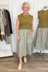 Front view of woman wearing Swagger Boutique’s Olive & Blue Striped Midi Skirt with Olive Sleeveless Sweater with clothing hanging in the background.