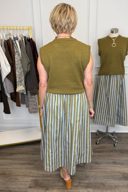 Back view of woman wearing Swagger Boutique’s Olive &amp; Blue Striped Midi Skirt with Olive Sleeveless Sweater with clothing hanging in the background.