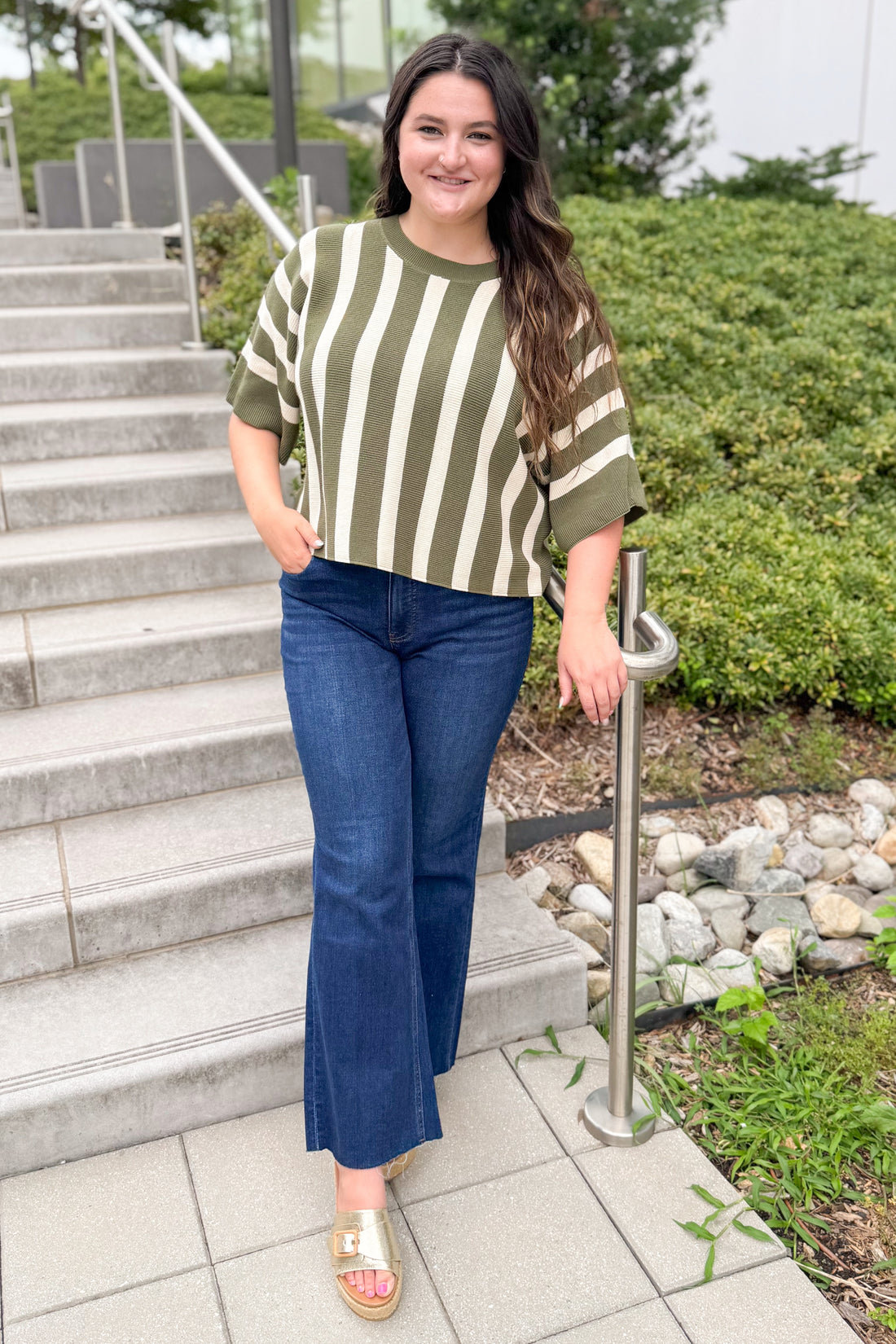Front view of woman wearing Swagger Boutique’s Olive &amp; Cream Striped Short Sleeve Sweater by Entro with jeans walking outside down a path.