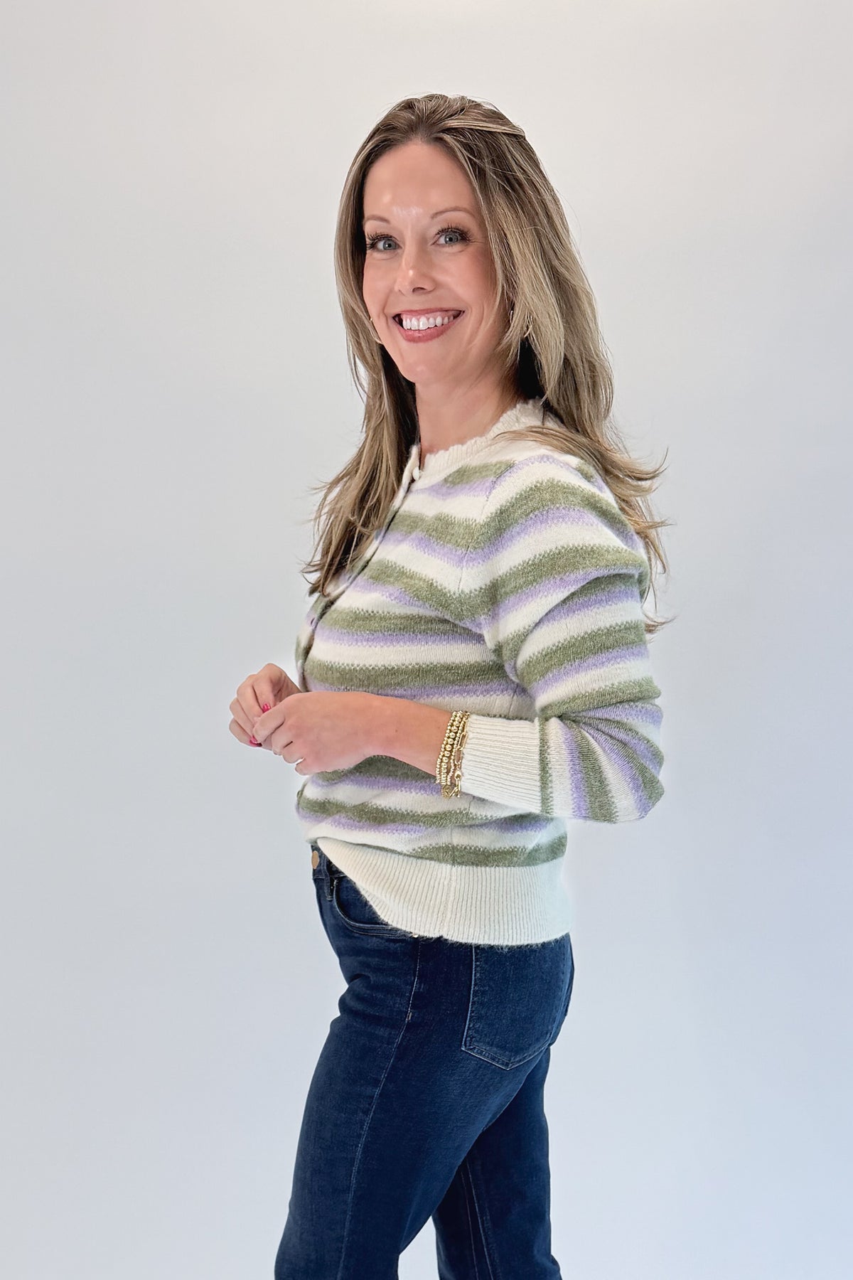 Side view of woman wearing Swagger Boutique’s Olive &amp; Lavendar Striped Button Up Cardigan with jeans against white studio background.