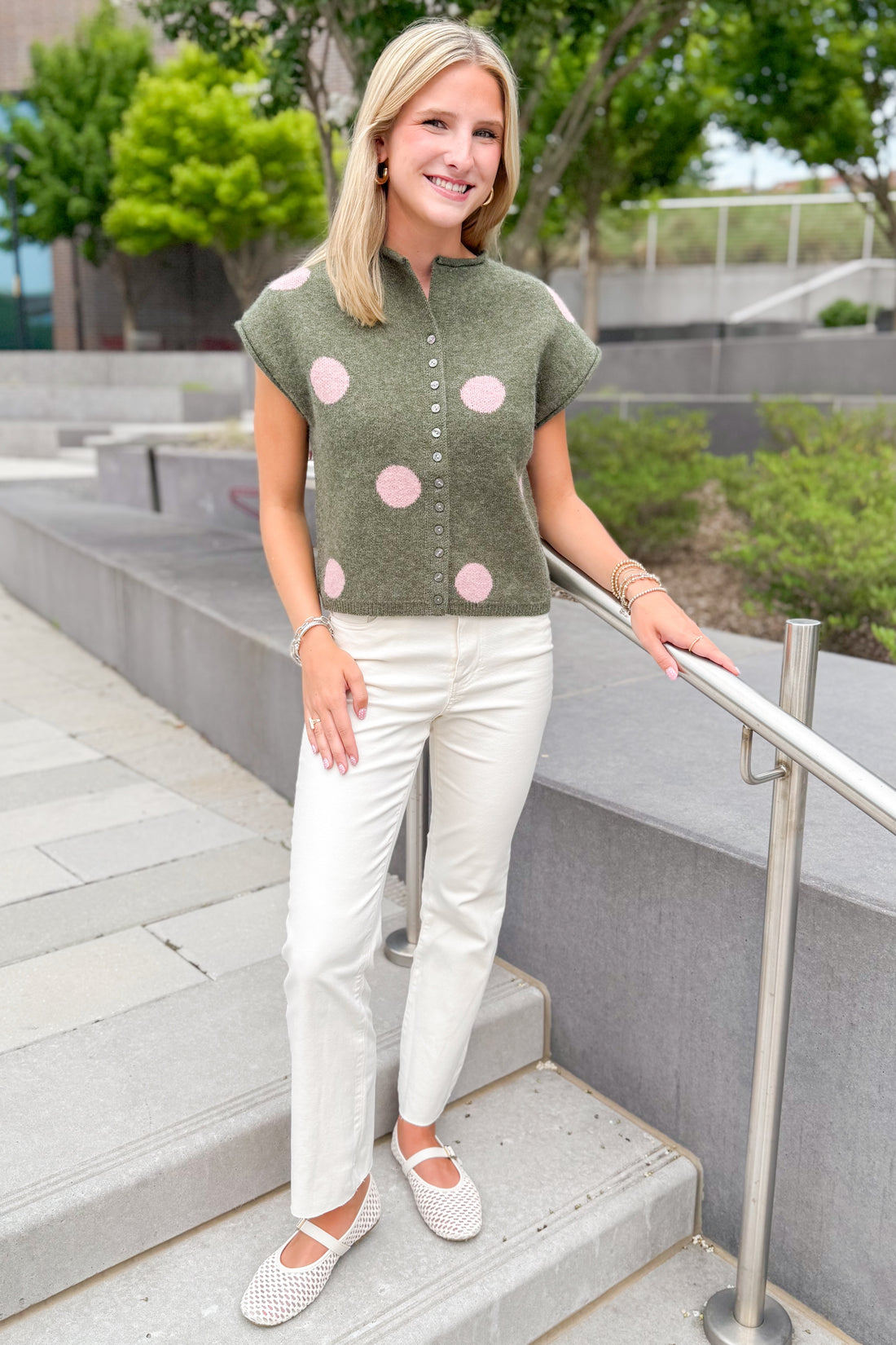 Front view of woman wearing Swagger Boutique’s Olive &amp; Pink Polka Dot Button Up Sweater by Entro with jeans walking down a staircase outside.