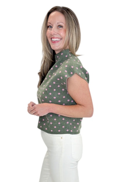 Side view of woman wearing Swagger Boutique’s Olive &amp; Pink Polka Dot Sleeveless Sweater by Entro with jeans against white studio background.