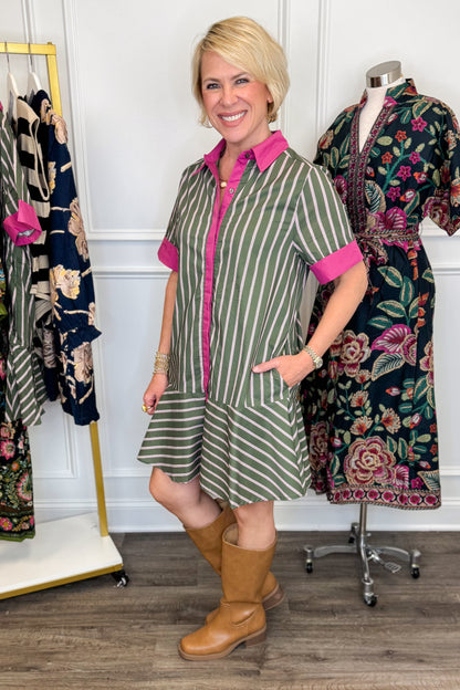Side view of woman wearing Swagger Boutique’s Olive &amp; Pink Striped Mini Dress by Entro with boots with clothing hanging in the background.