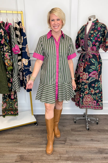 Front view of woman wearing Swagger Boutique’s Olive &amp; Pink Striped Mini Dress by Entro with boots with clothing hanging in the background.