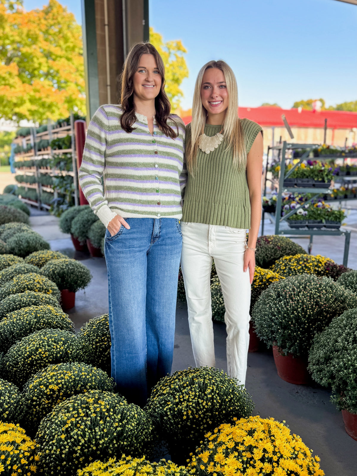 Front view of women wearing Swagger Boutique’s Olive Ribbed Sleeveless Sweater and Olive &amp; Lavender Striped Button Up Cardigan with jeans at a garden center.