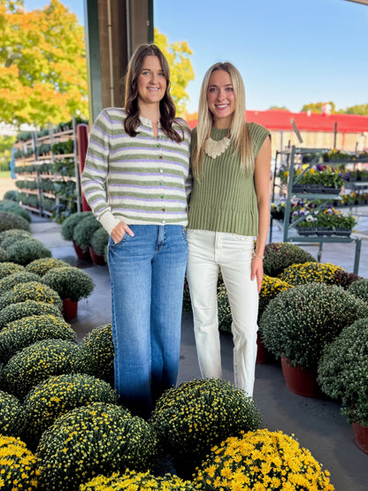 Front view of women wearing Swagger Boutique’s Olive Ribbed Sleeveless Sweater and Olive &amp; Lavender Striped Button Up Cardigan with jeans at a garden center.