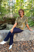 Front view of woman wearing Swagger Boutique’s Olive Velvet Ruffle Neck Top with jeans sitting at a park outside.