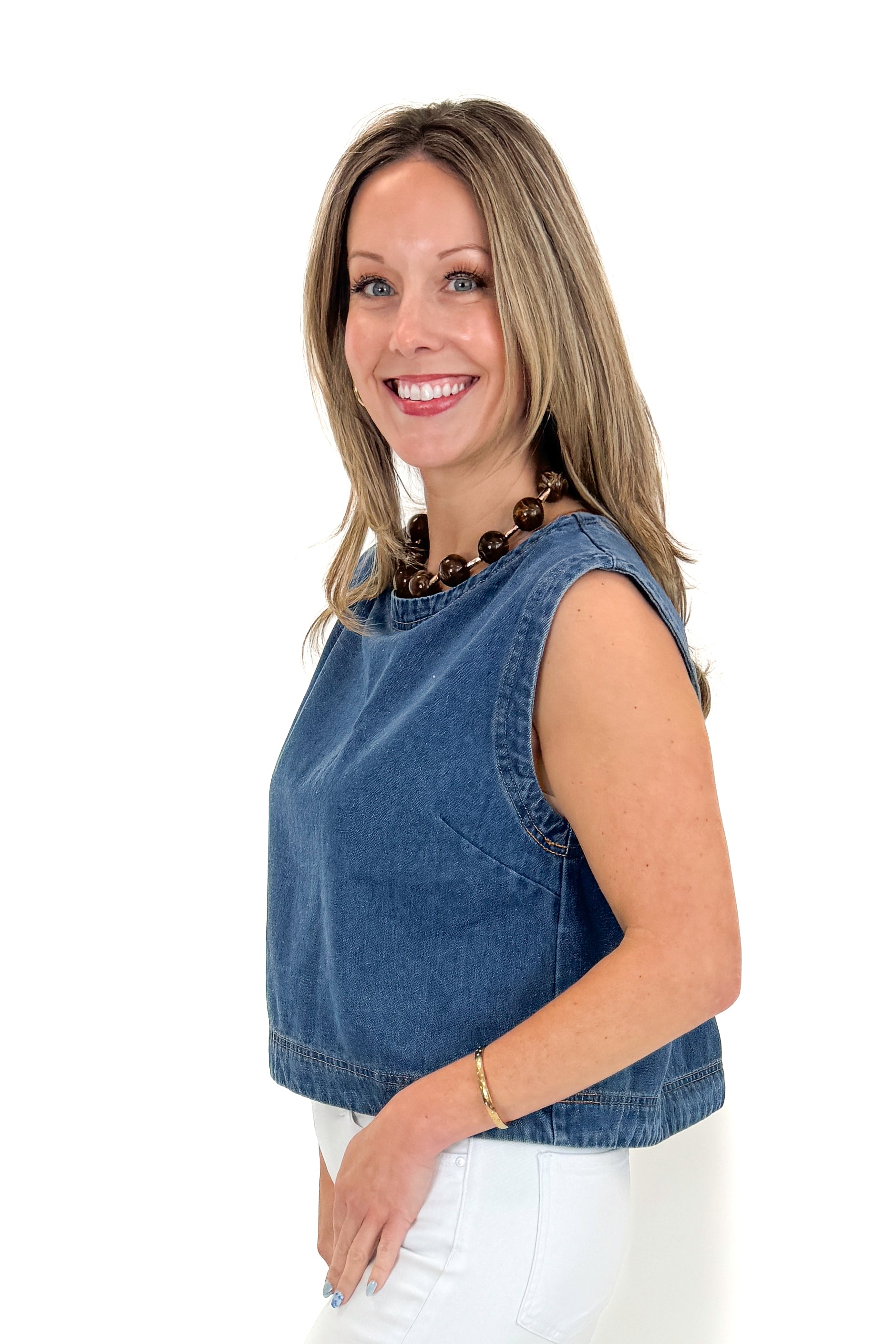 Side view of woman wearing Medium Wash Denim Top with jeans against white studio background.