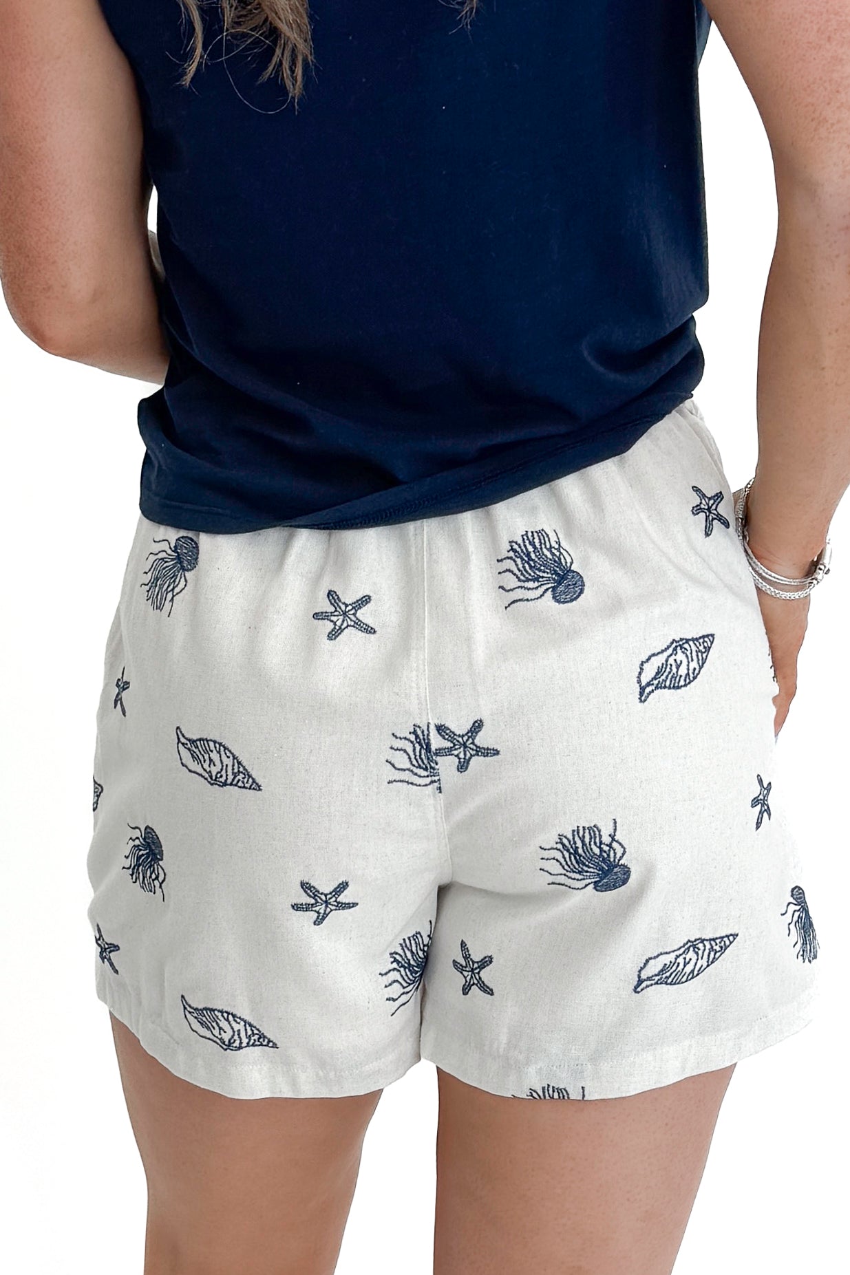 Back view of woman wearing Linen &amp; Navy Shell Embroidered Skort by Entro with top against white studio background.