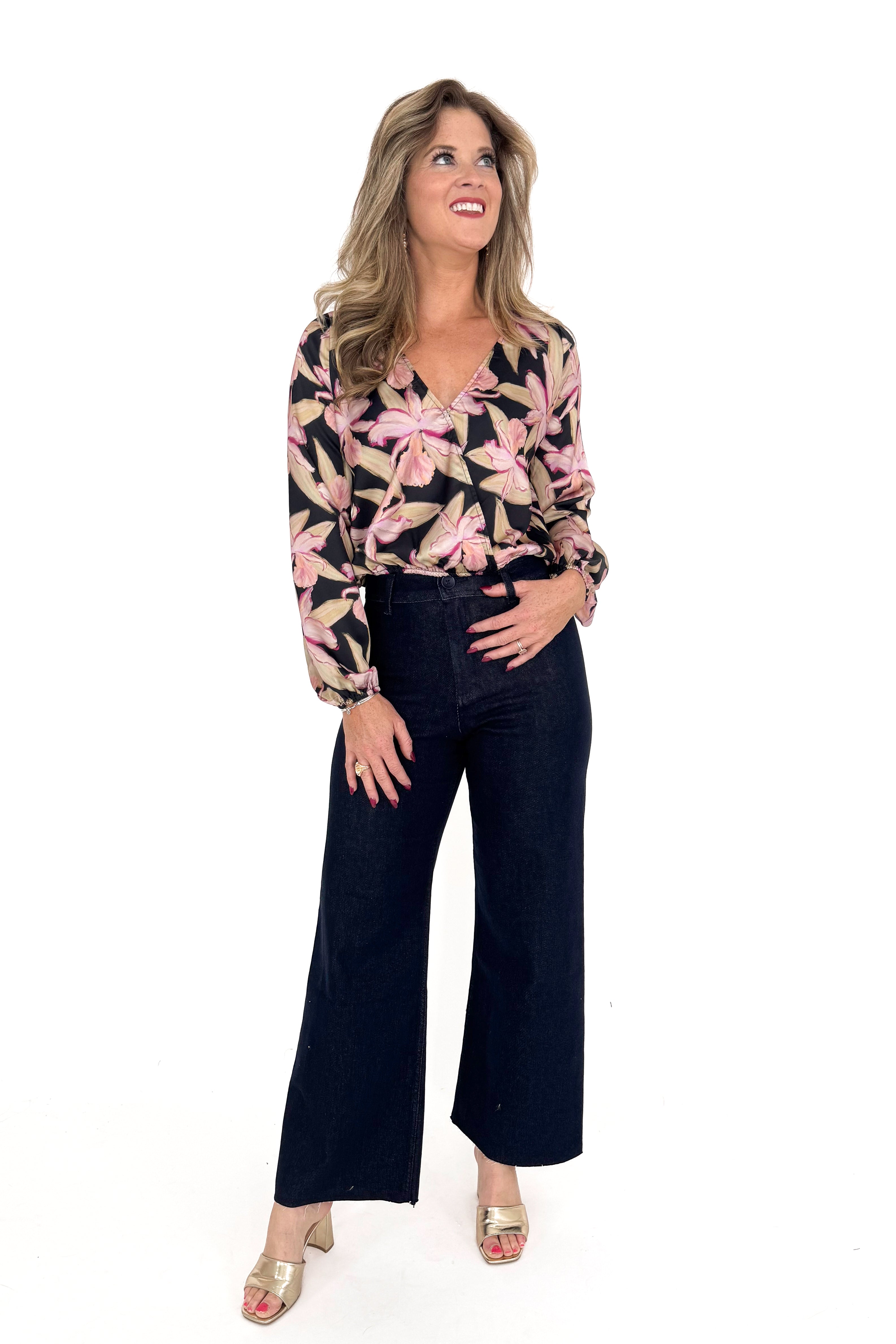 Woman in a floral blouse and jeans with white studio background.