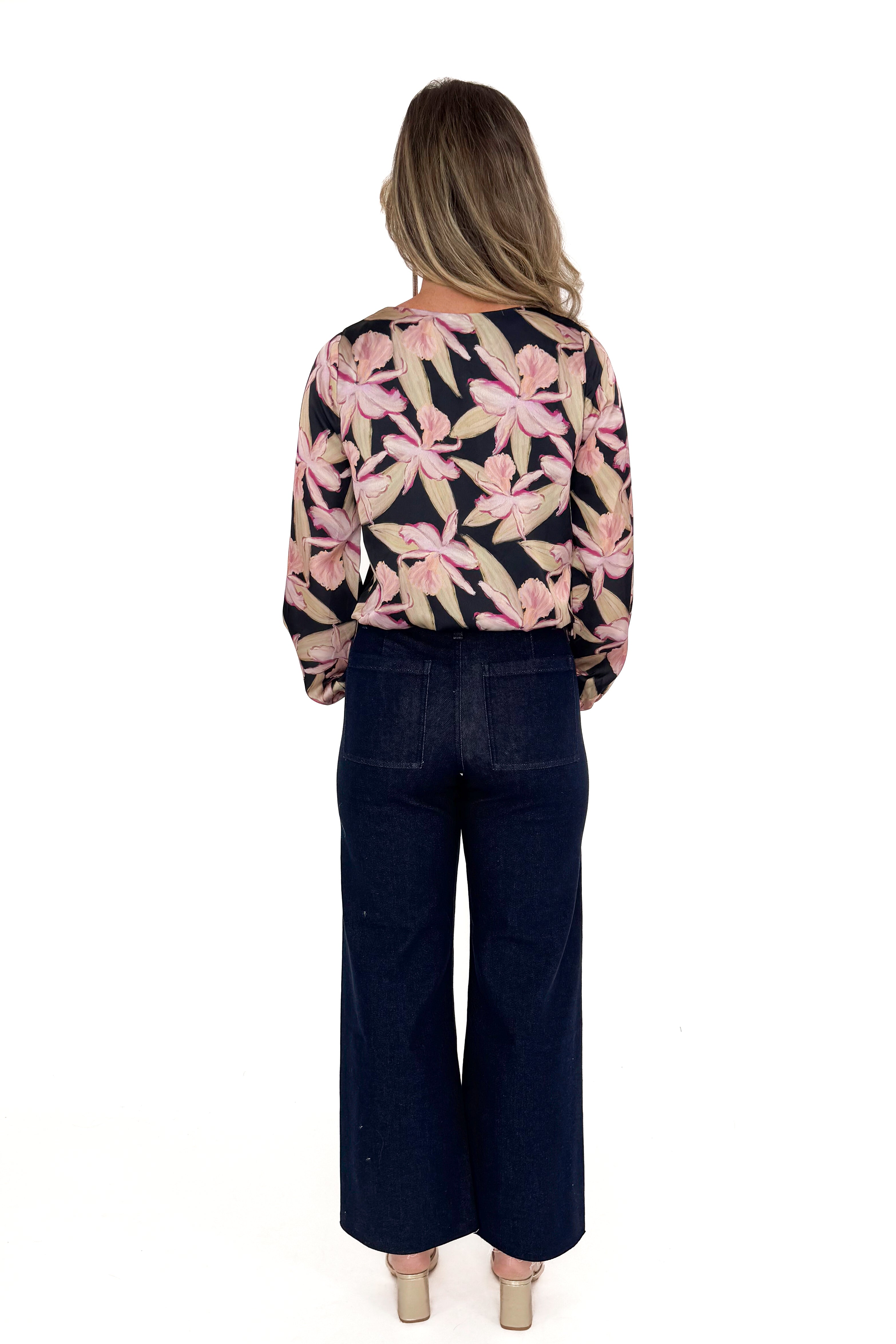 Back view of woman in a floral blouse and jeans with white studio background.