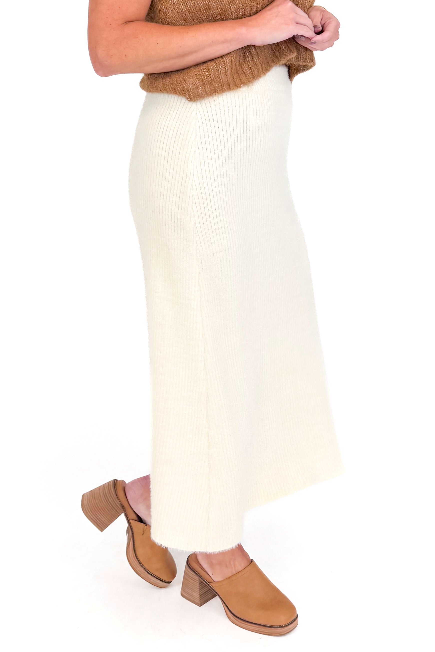 Studio picture of a woman in Cream Eyelash Midi Skirt and camel color sleeveless sweater against a white background.