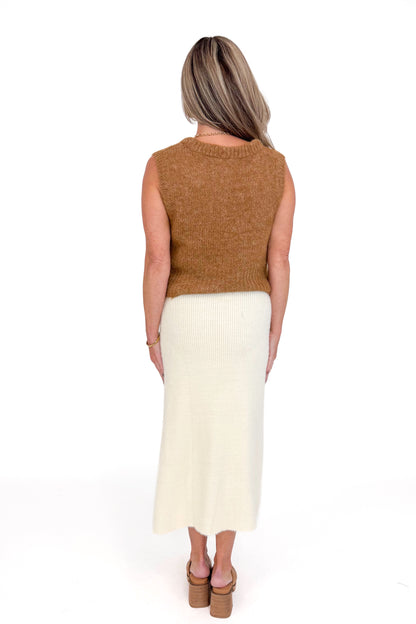 Studio picture of a woman in Cream Eyelash Midi Skirt and camel color sleeveless sweater against a white background.