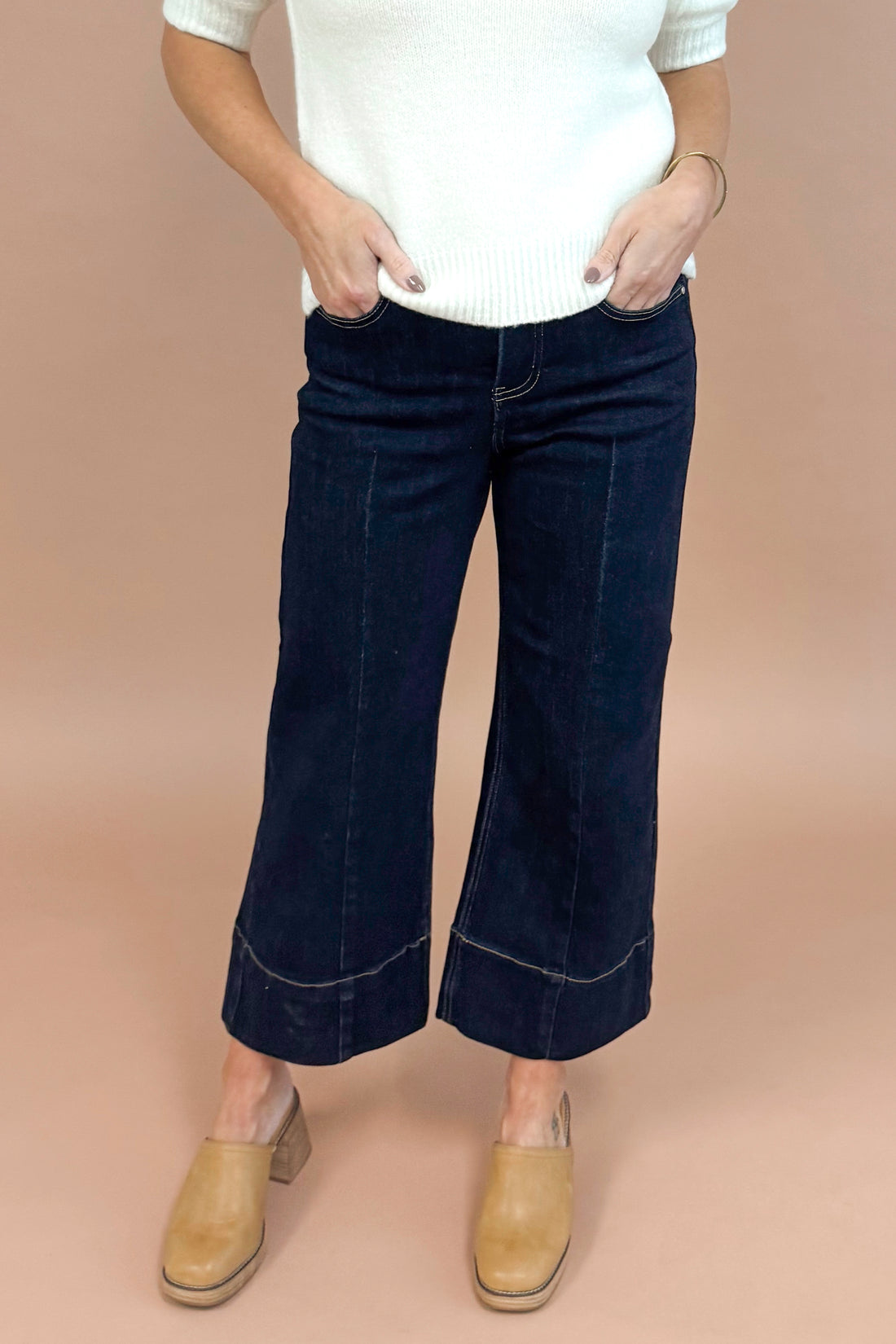 Person wearing navy blue flared pants and a white top on a beige background