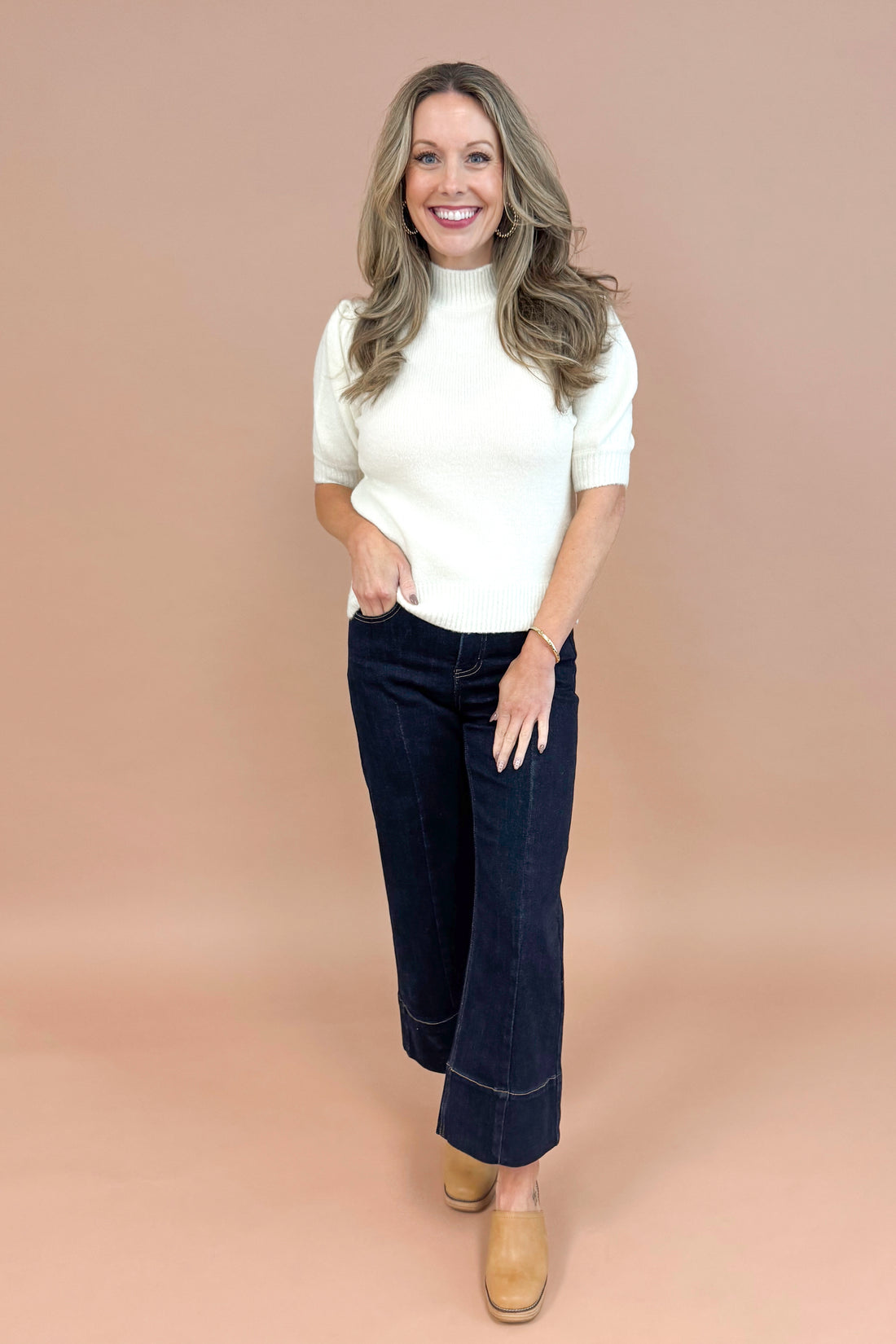 Woman wearing a white top and dark blue jeans on a beige background