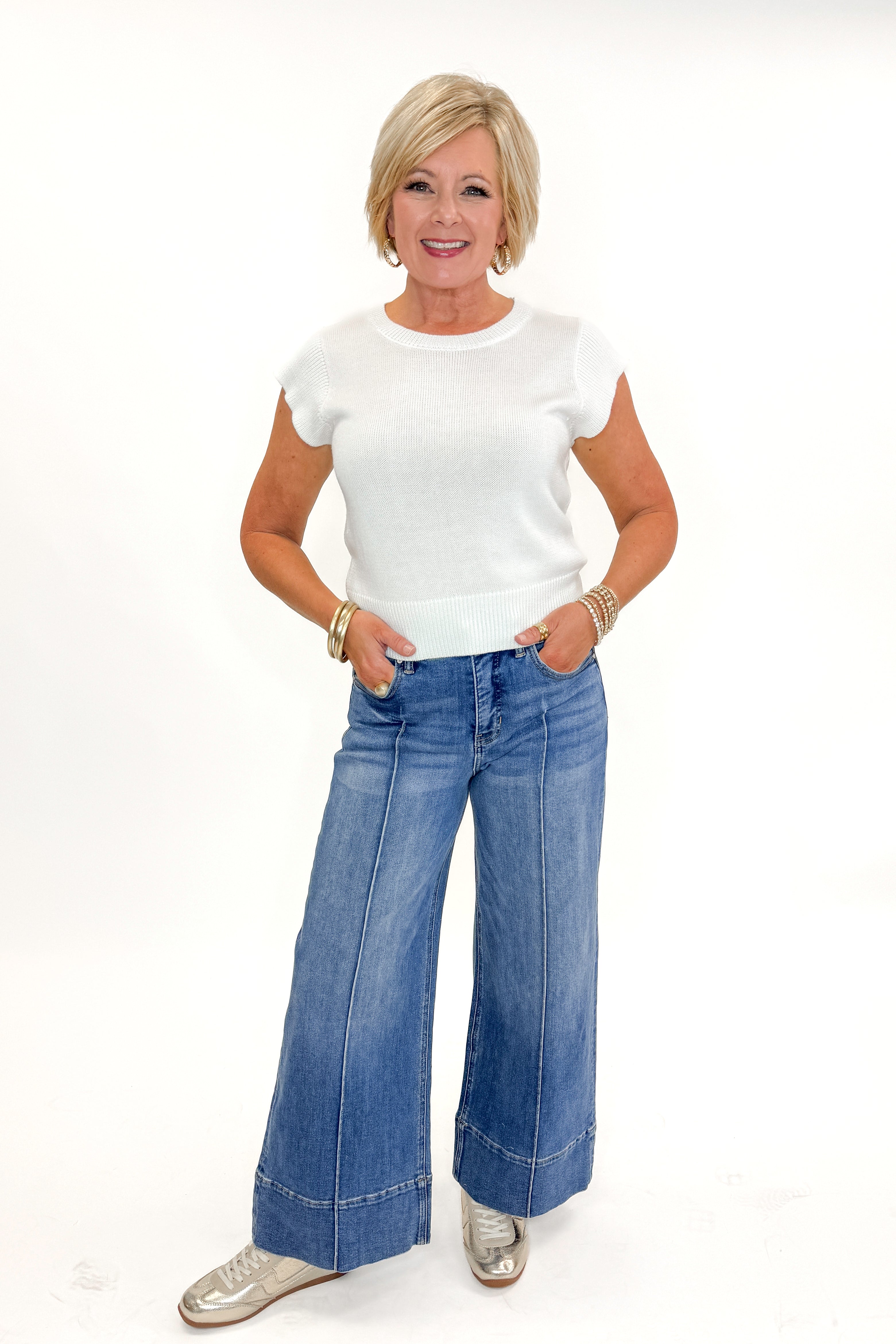 Front view of woman wearing Medium Wash Pintuck Detail Jeans by Risen with white sweater against white studio background.