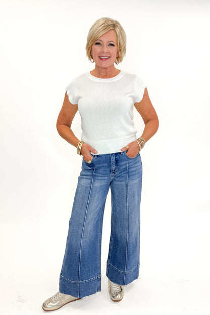 Front view of woman wearing Medium Wash Pintuck Detail Jeans by Risen with white sweater against white studio background.