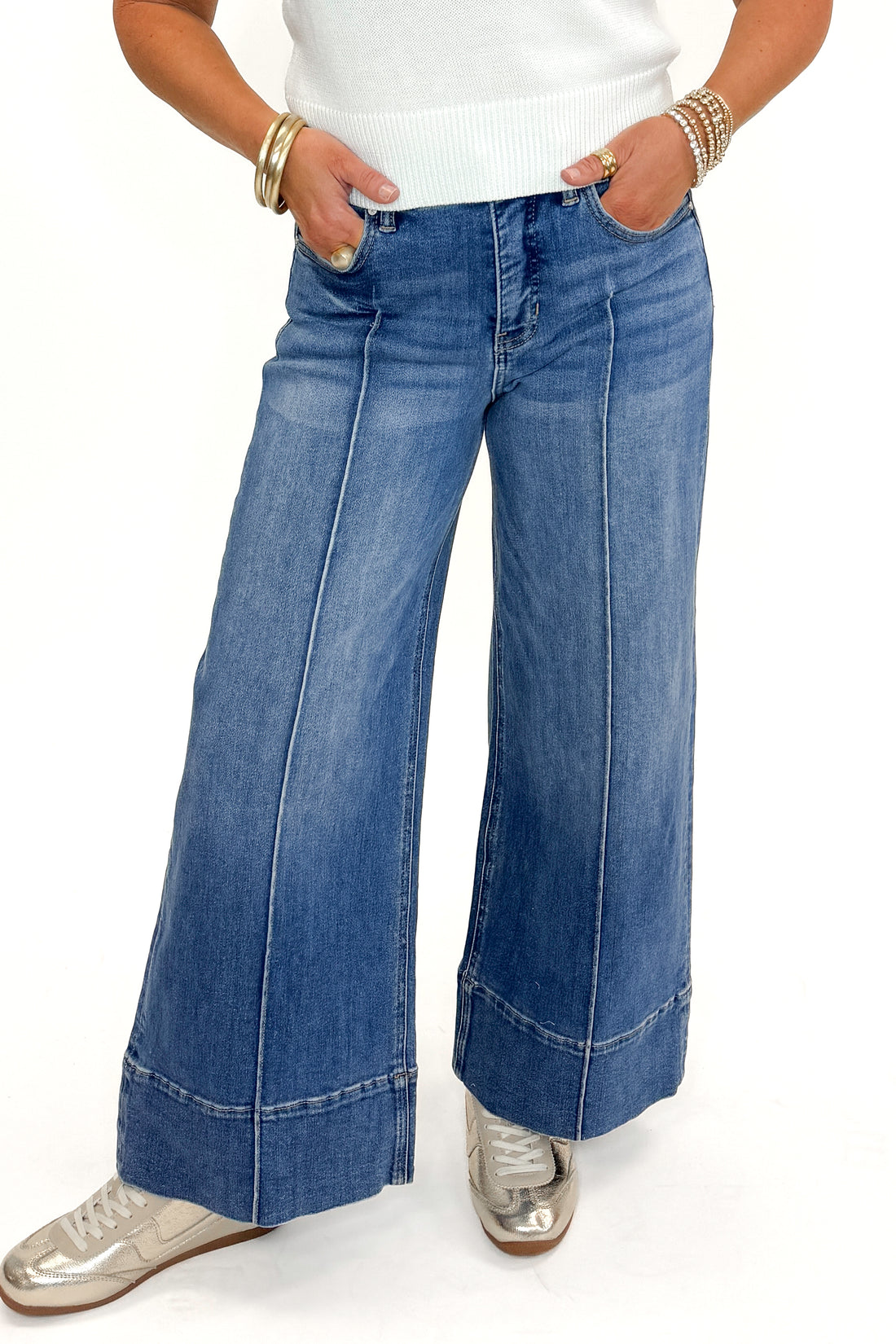 Front view of woman wearing Medium Wash Pintuck Detail Jeans by Risen with white sweater against white studio background.