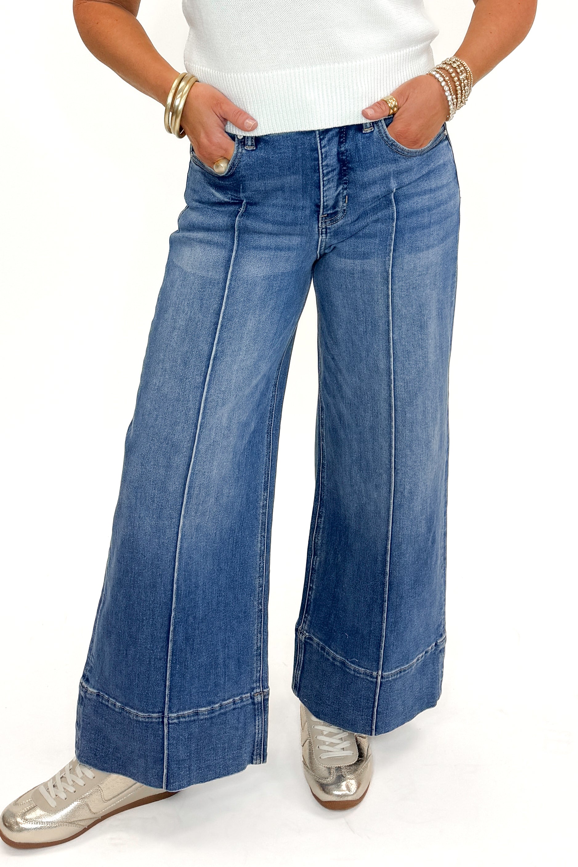 Front view of woman wearing Medium Wash Pintuck Detail Jeans by Risen with white sweater against white studio background.