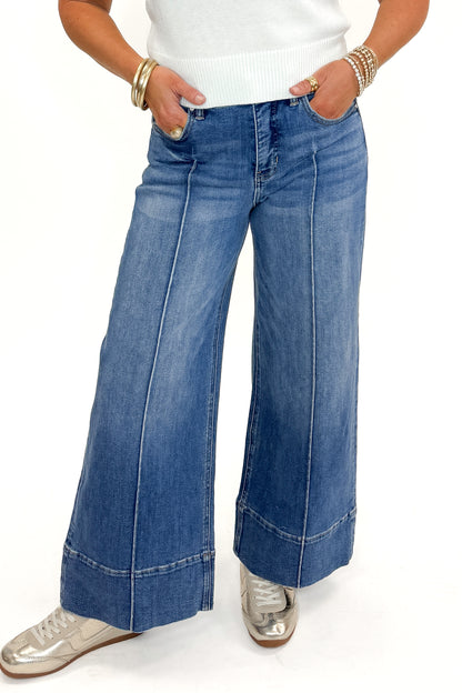 Front view of woman wearing Medium Wash Pintuck Detail Jeans by Risen with white sweater against white studio background.