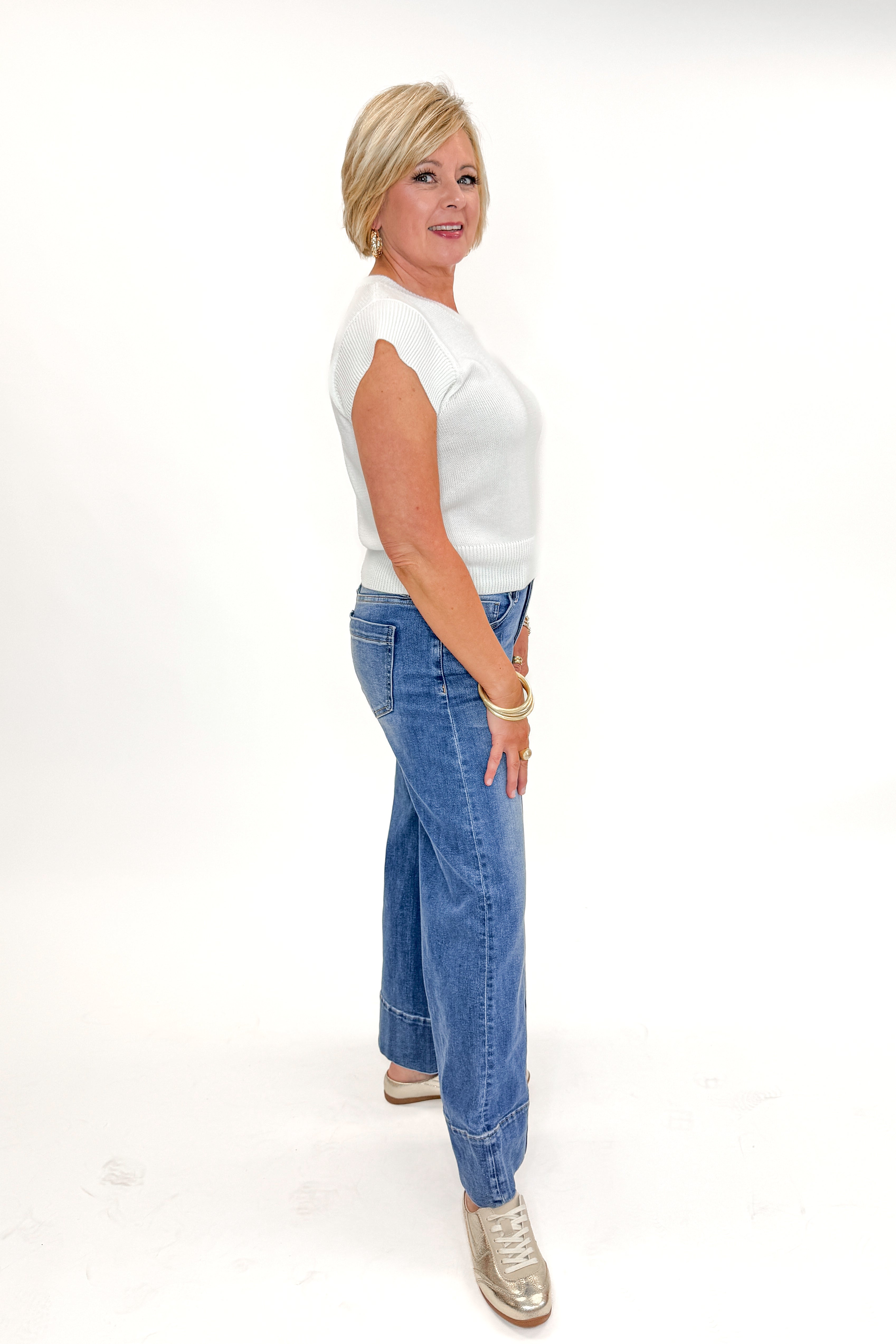 Side view of woman wearing Medium Wash Pintuck Detail Jeans by Risen with white sweater against white studio background.