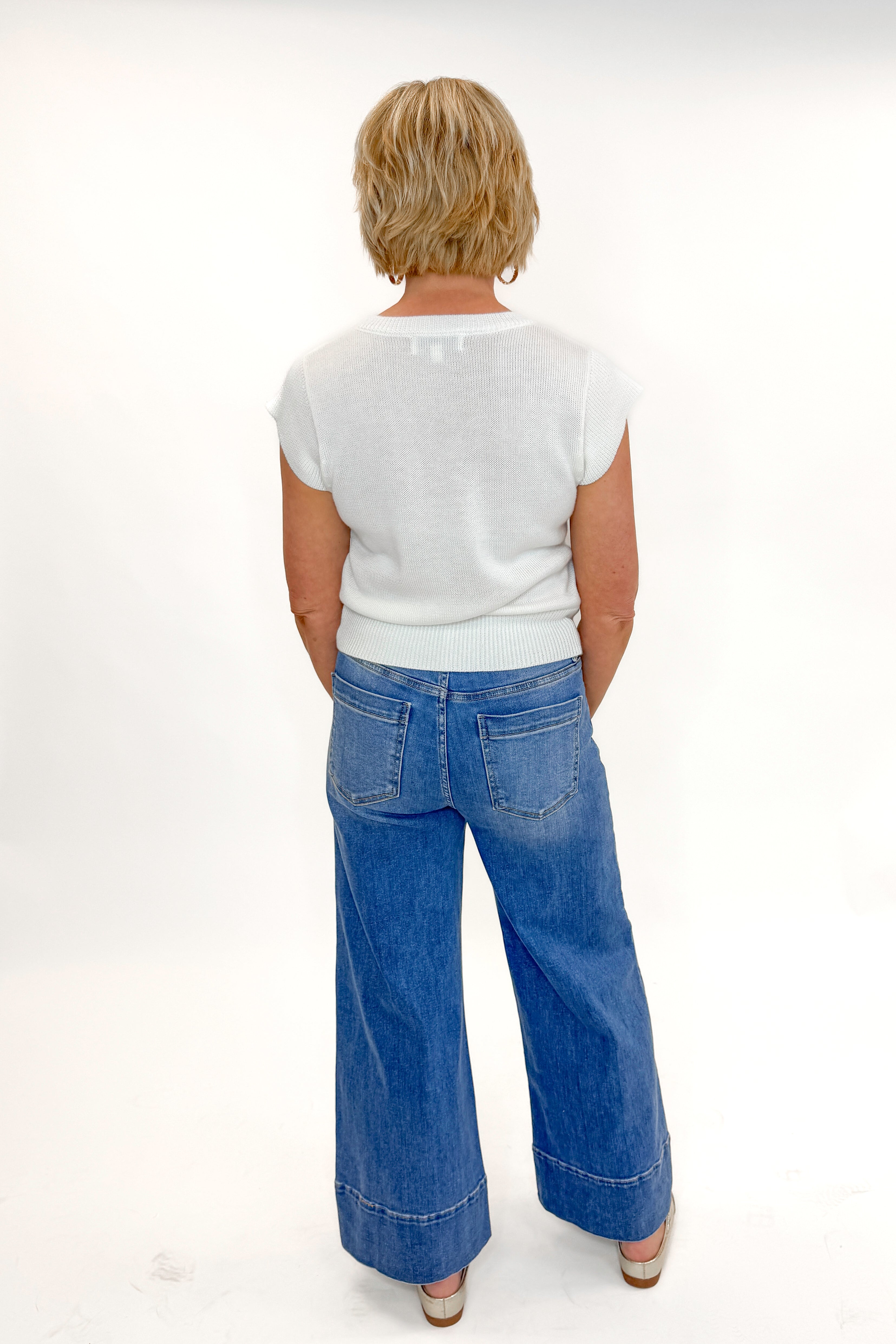 Back view of woman wearing Medium Wash Pintuck Detail Jeans by Risen with white sweater against white studio background.