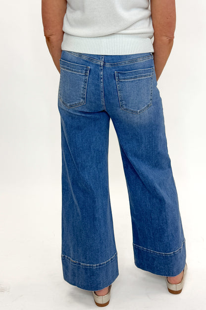 Back view of woman wearing Medium Wash Pintuck Detail Jeans by Risen with white sweater against white studio background.
