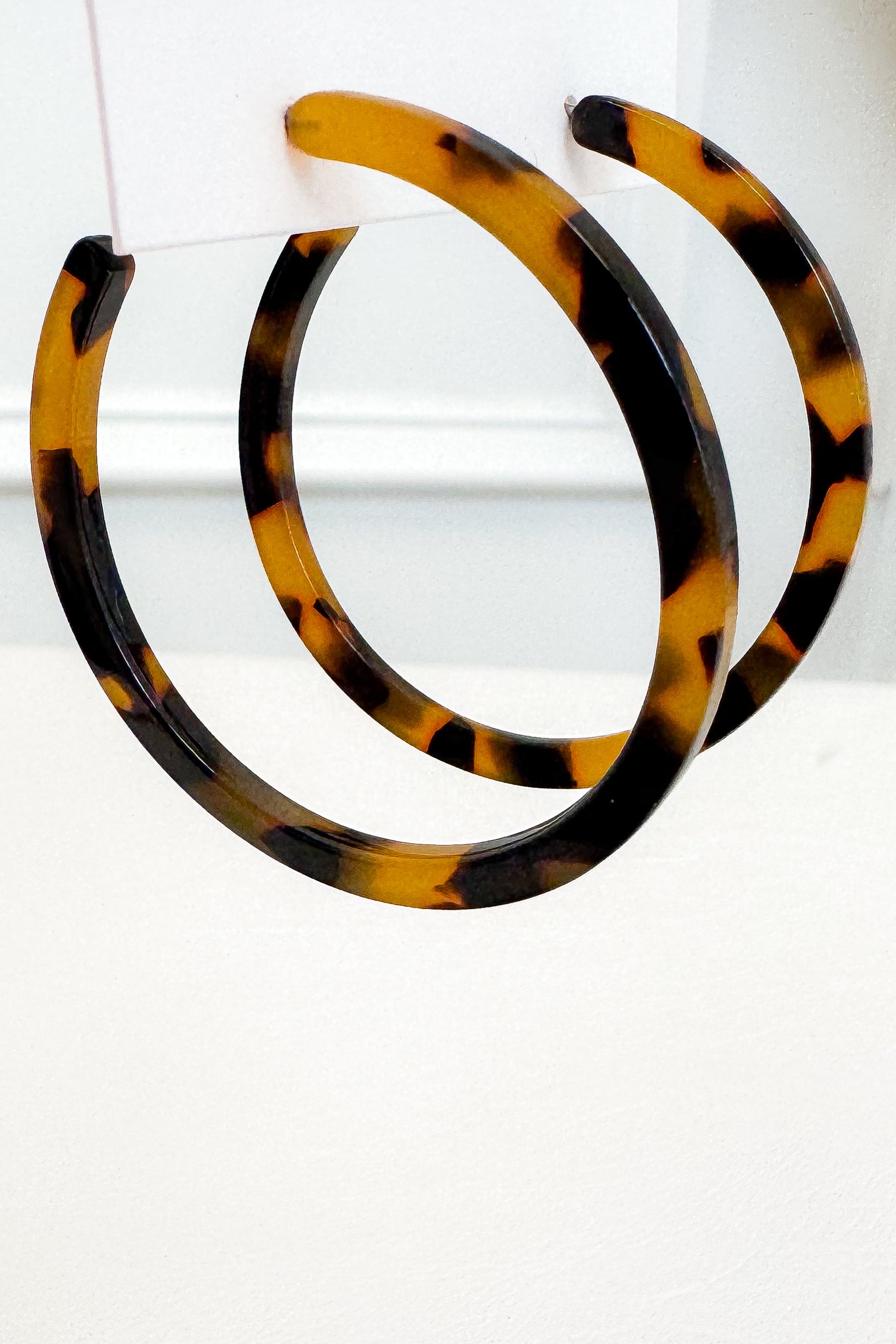A pair of large tortoiseshell hoop earrings with a glossy amber-brown and black pattern, displayed against a clean white background.