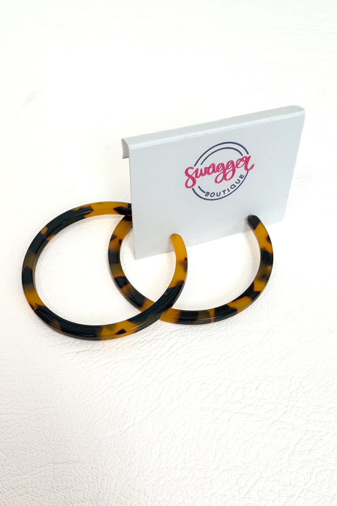 Tortoiseshell hoop earrings displayed on a white stand with the &