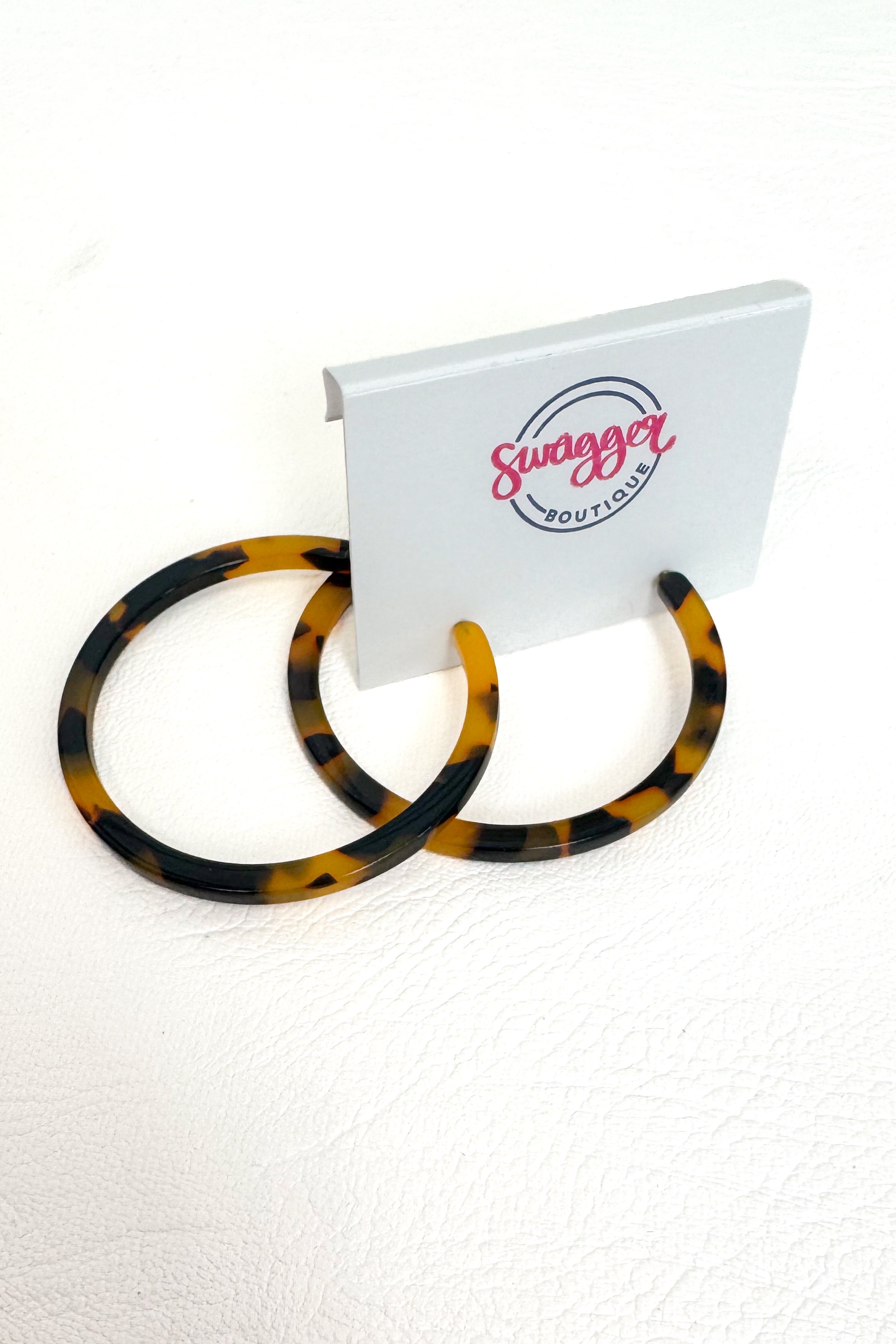 Tortoiseshell hoop earrings displayed on a white stand with the &