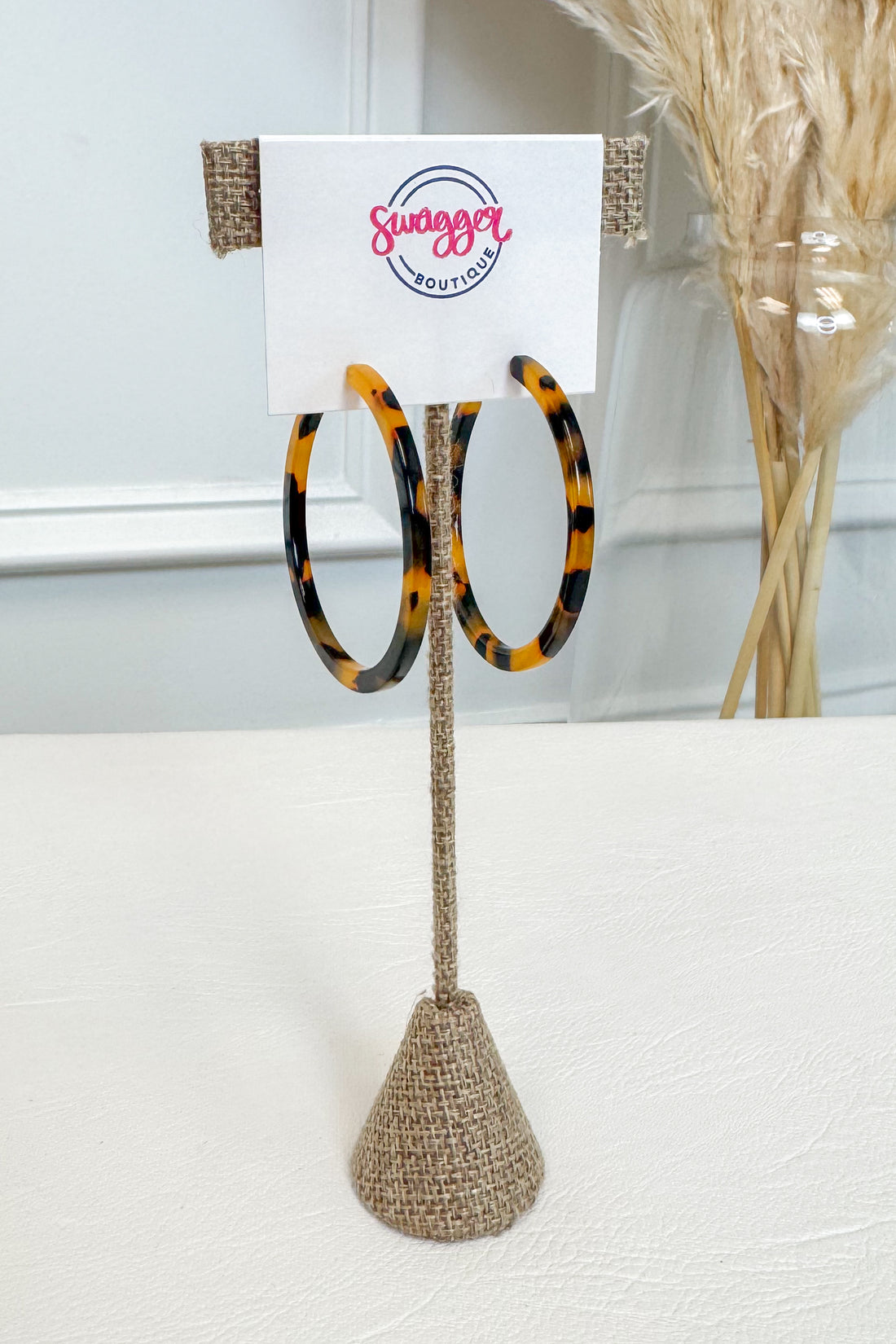 Tortoiseshell hoop earrings displayed on a burlap-covered stand with a white card labeled &